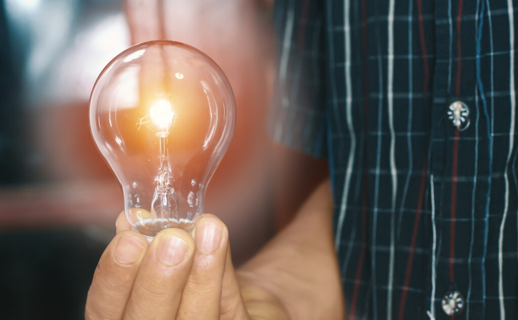 como reduzir o consumo de energia eletrica na sua residencia Homem com lâmpada na mão pensando em como reduzir o consumo de energia